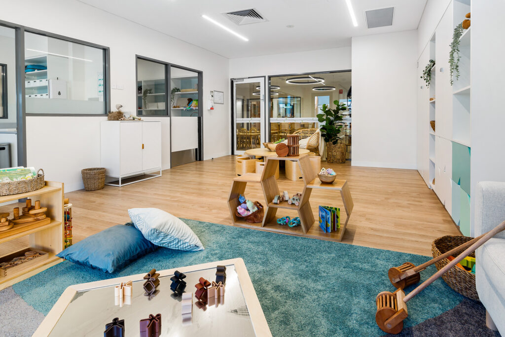 Nido Riverton Living room with toys, wooden floor, transparent door, carpet and pillows