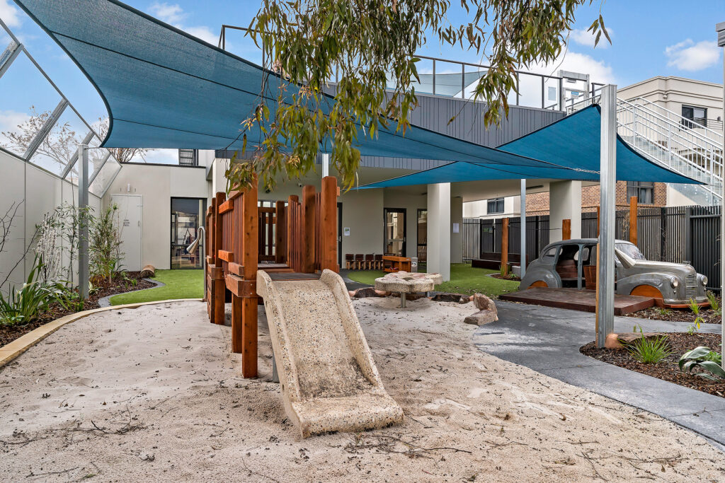 Nido Essendon Terrace area including stone slide with wooden stairs, old car, small wooden chairs, stone pillars and green grass