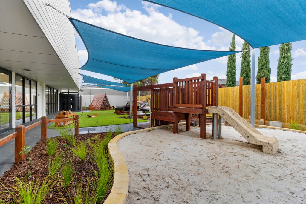 Nido Avondale Heights Area with green grass, small slide attch with wooden strings, center area covered with mud and small stone platform