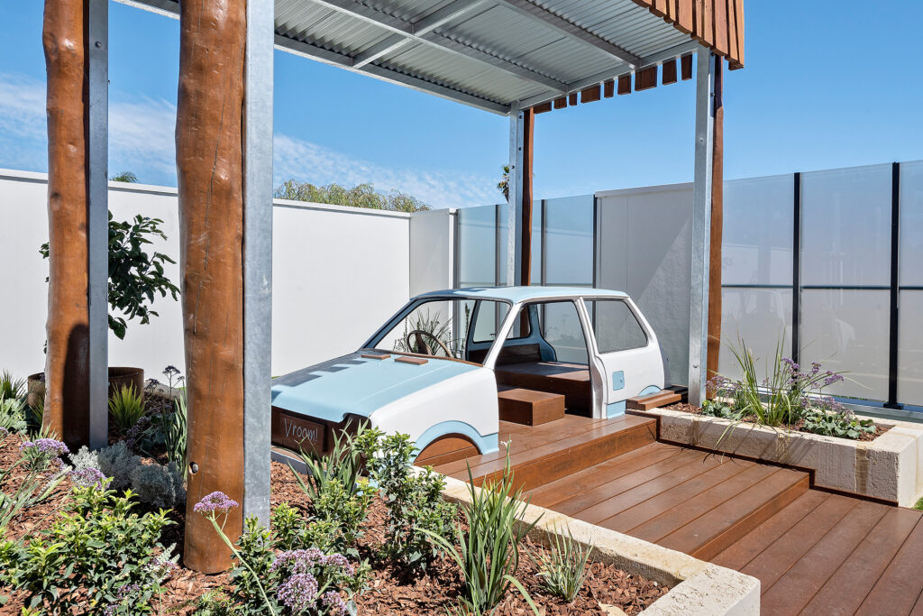 A blue car shaped play structure is situated under a metal canopy at Nido Thornlie childcare centre
