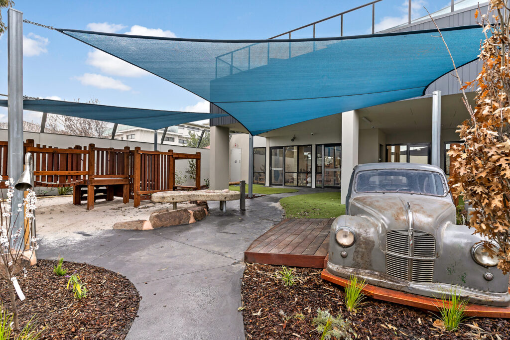 Nido Essendon Terrace area with small stone platform, old damaged car, Wooden strings and white flowers plant
