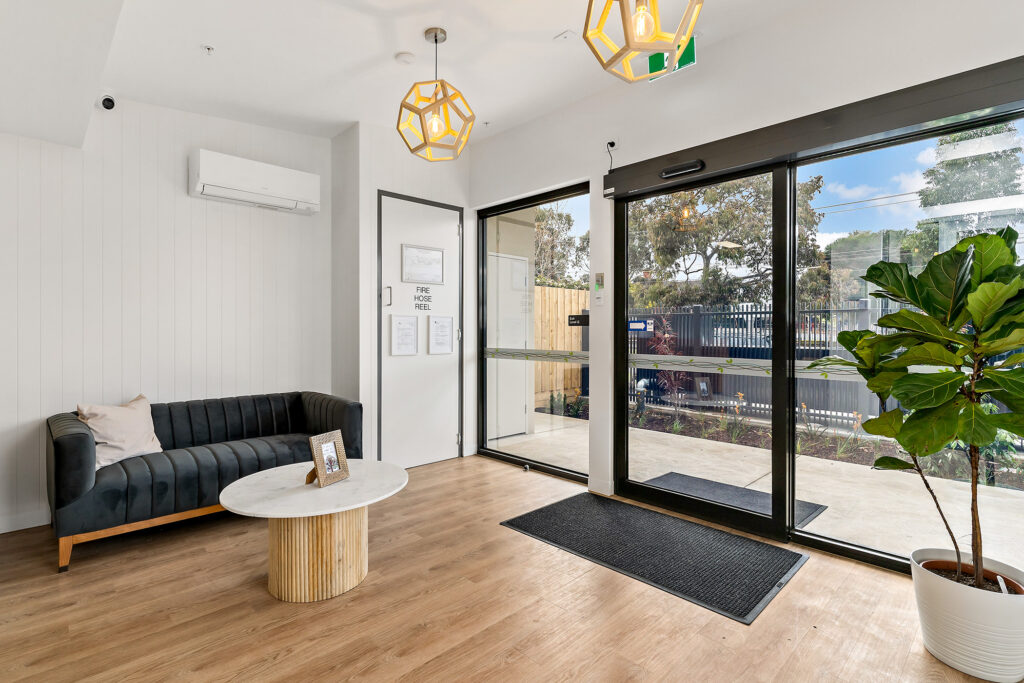 Nido Essendon Living room with transparent doors, sofa, pillow, artificial plant, photo frame and door mat