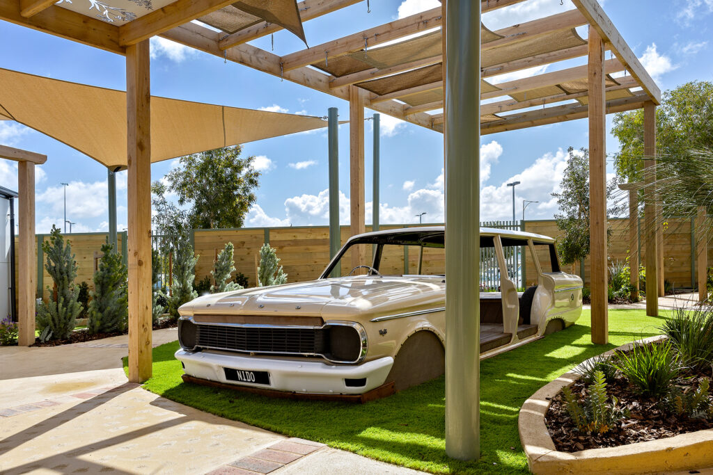 A car under a canopy in the garden of the Nido Childcare Centre, surrounded by greenery