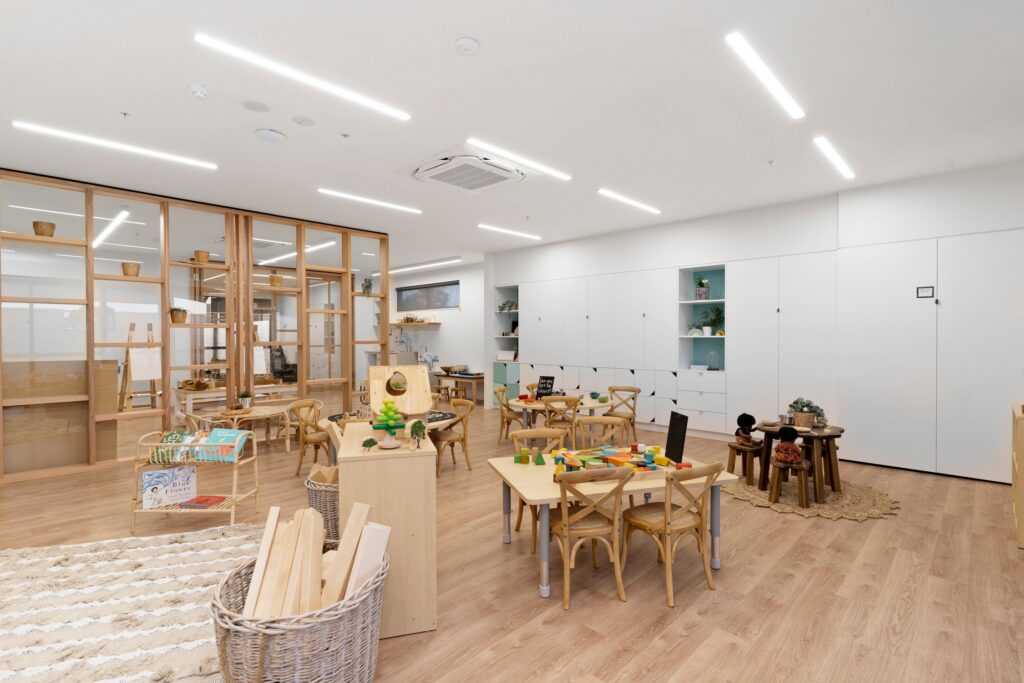 Nido Avondale Heights Living area with small wooden chairs, table, wooden sticks in basket and cupboard with drawers