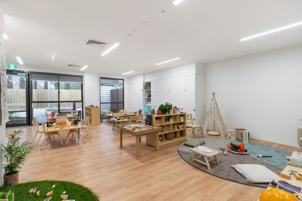 Nido Avondale Heights Living room with Small wooden table, chairs, stand with boxes, carpet, toys, books, grass carpet and artificial plant
