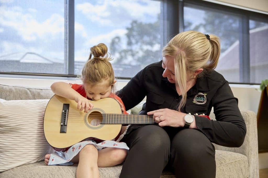 Child and Early Learning teacher playing guitar at Nido Belair